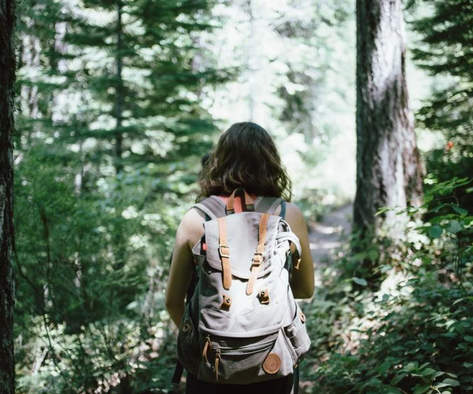 Una donna di spalle con lo zaino su un sentiero nel bosco
