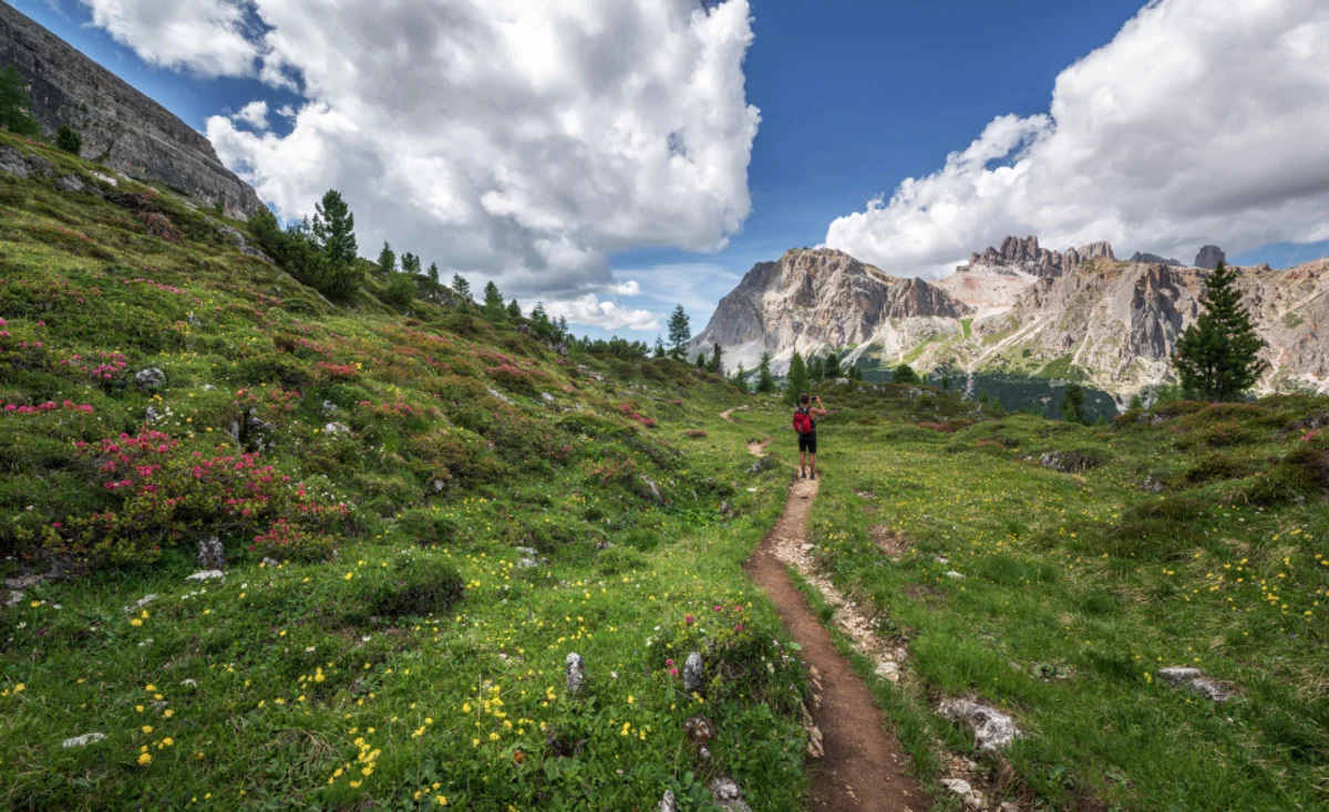 Un sentiero tra i prati sotto le Dolomiti, con un'escursionista lontana
